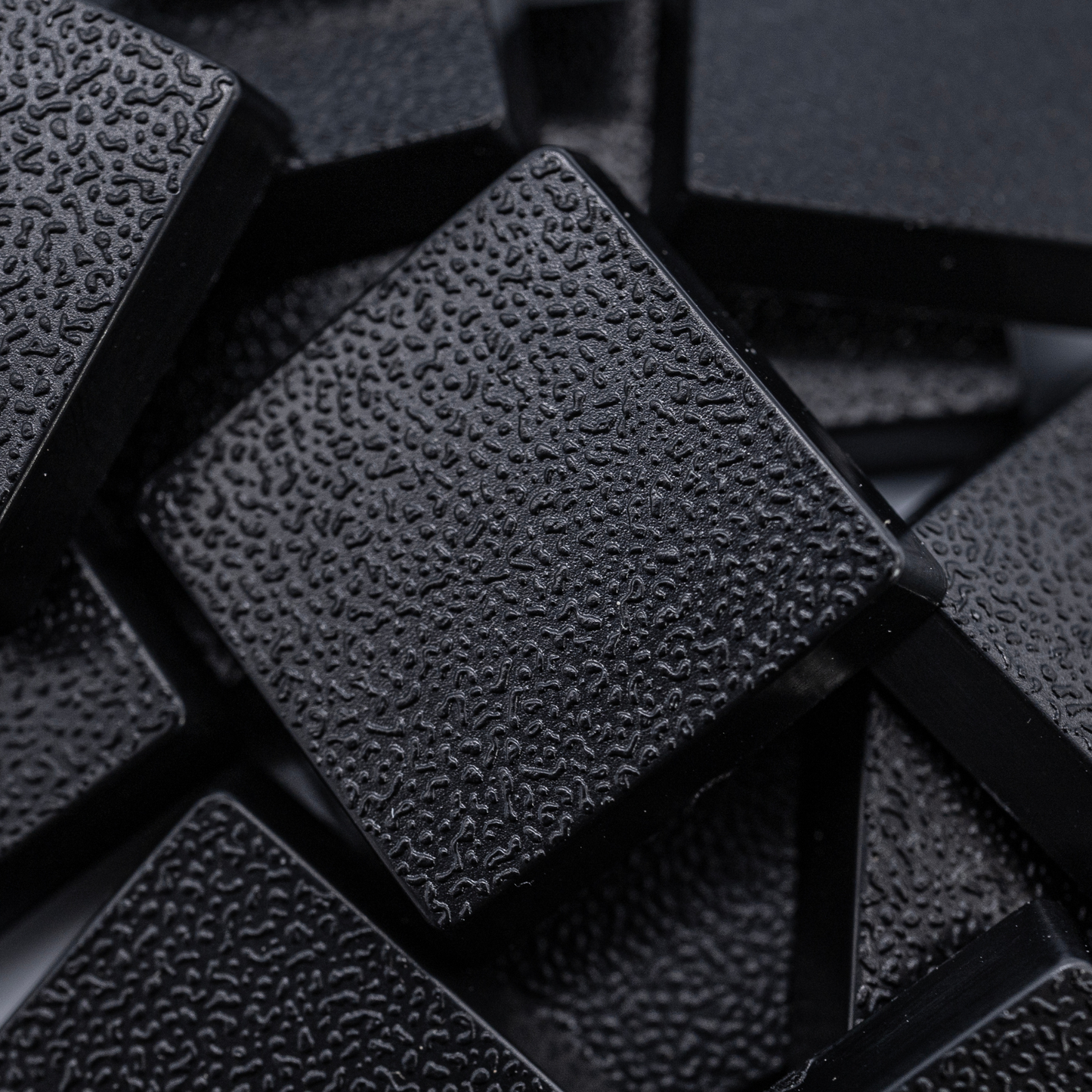 Close-up of black 20mm square plastic miniature bases showing textured top surfaces for tabletop wargaming, RPG figures, rank-and-file units, conversions, and hobby basing projects.