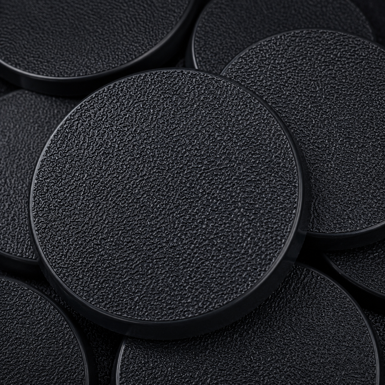 Close-up of black 50mm round plastic miniature bases showing textured top surfaces for tabletop wargaming, RPG monsters, conversions, and hobby basing projects.