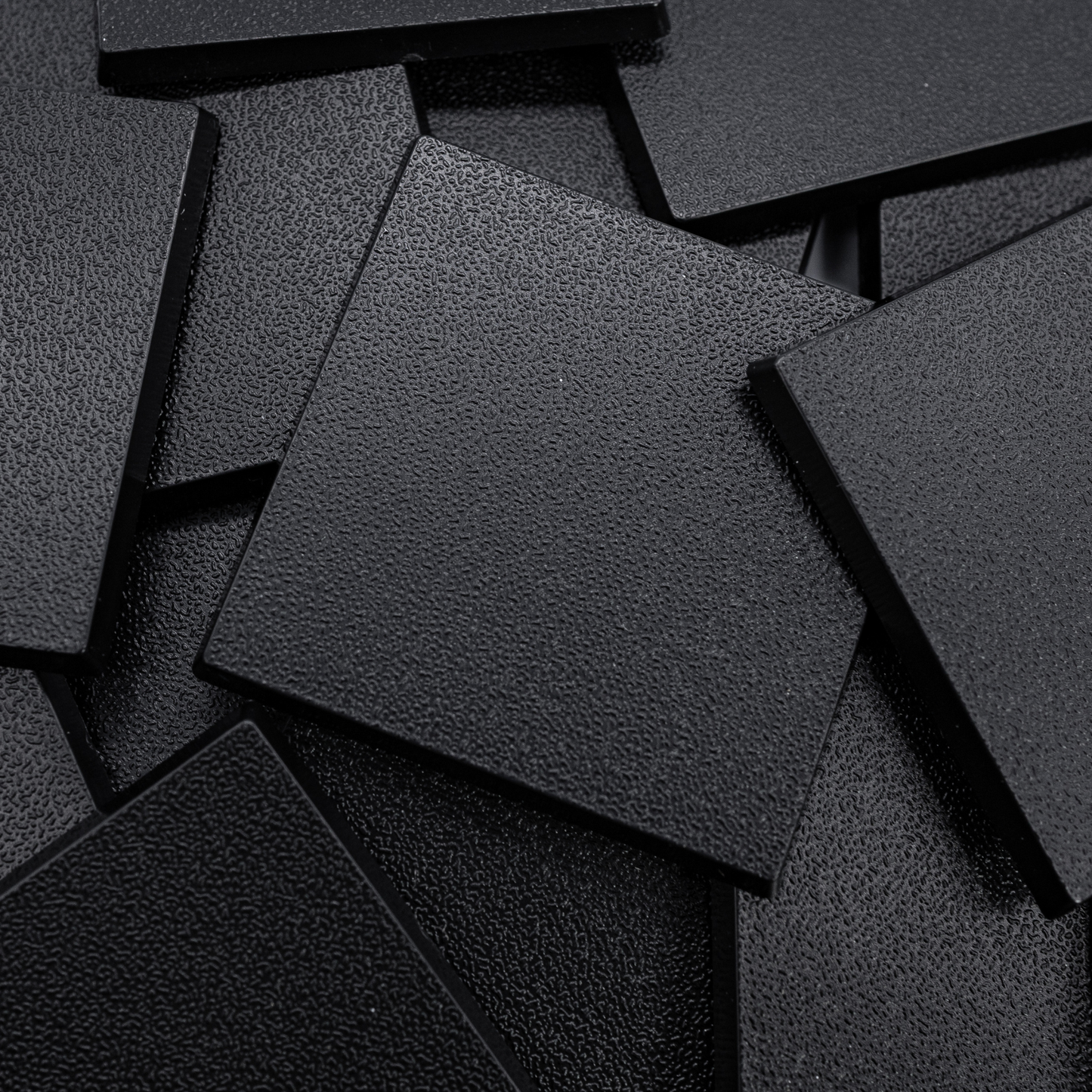 Close-up of black 50mm square plastic miniature bases showing textured top surfaces for tabletop wargaming, RPG monsters, rank-and-file units, conversions, and hobby basing projects.