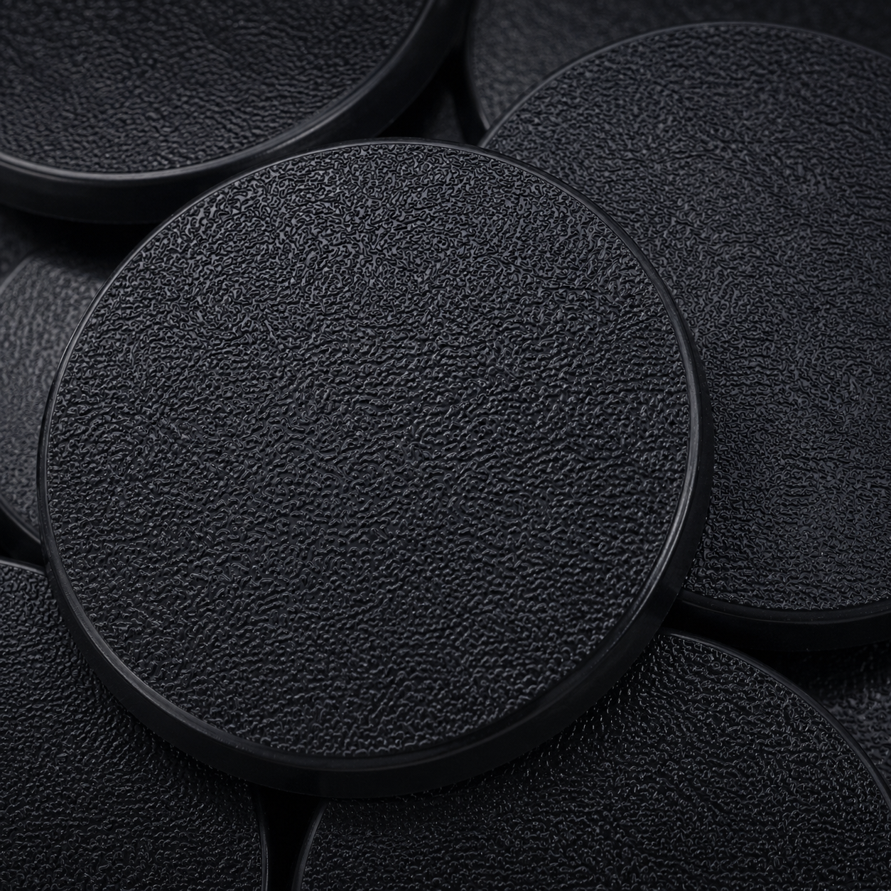 Close-up of black 60mm round plastic miniature bases showing textured top surfaces for tabletop wargaming, RPG monsters, conversions, and hobby basing projects.