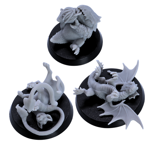 Top view of three unpainted baby monster miniatures on round bases, including curled and reclining creature poses.