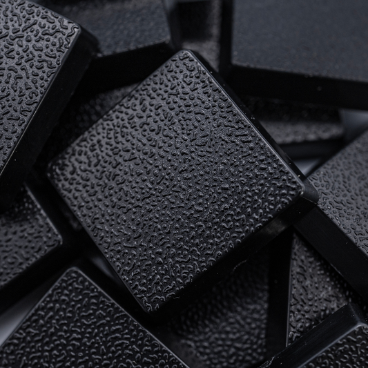 Close-up of black 20mm square plastic miniature bases showing textured top surfaces for tabletop wargaming, RPG figures, rank-and-file units, conversions, and hobby basing projects.