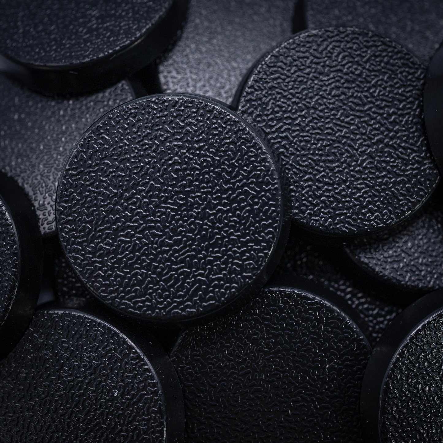 Close-up of black 25mm round plastic miniature bases showing textured top surfaces for tabletop wargaming, RPG figures, and hobby basing projects.