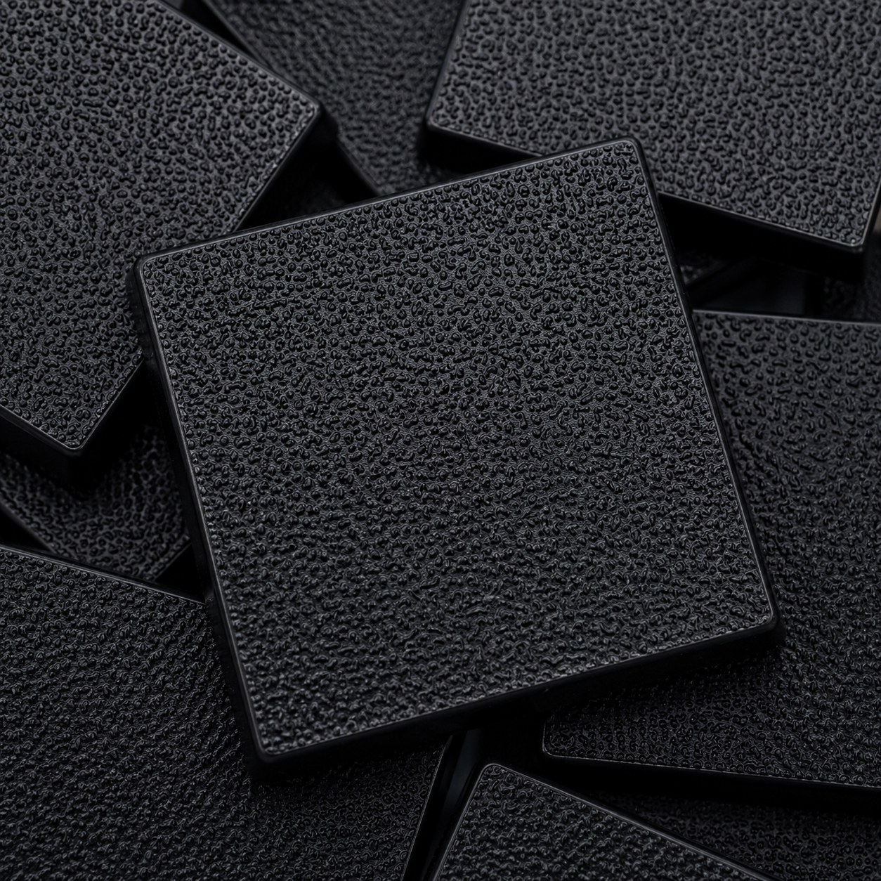 Close-up of black 32mm square plastic miniature bases showing textured top surfaces for tabletop wargaming, RPG figures, rank-and-file units, conversions, and hobby basing projects.