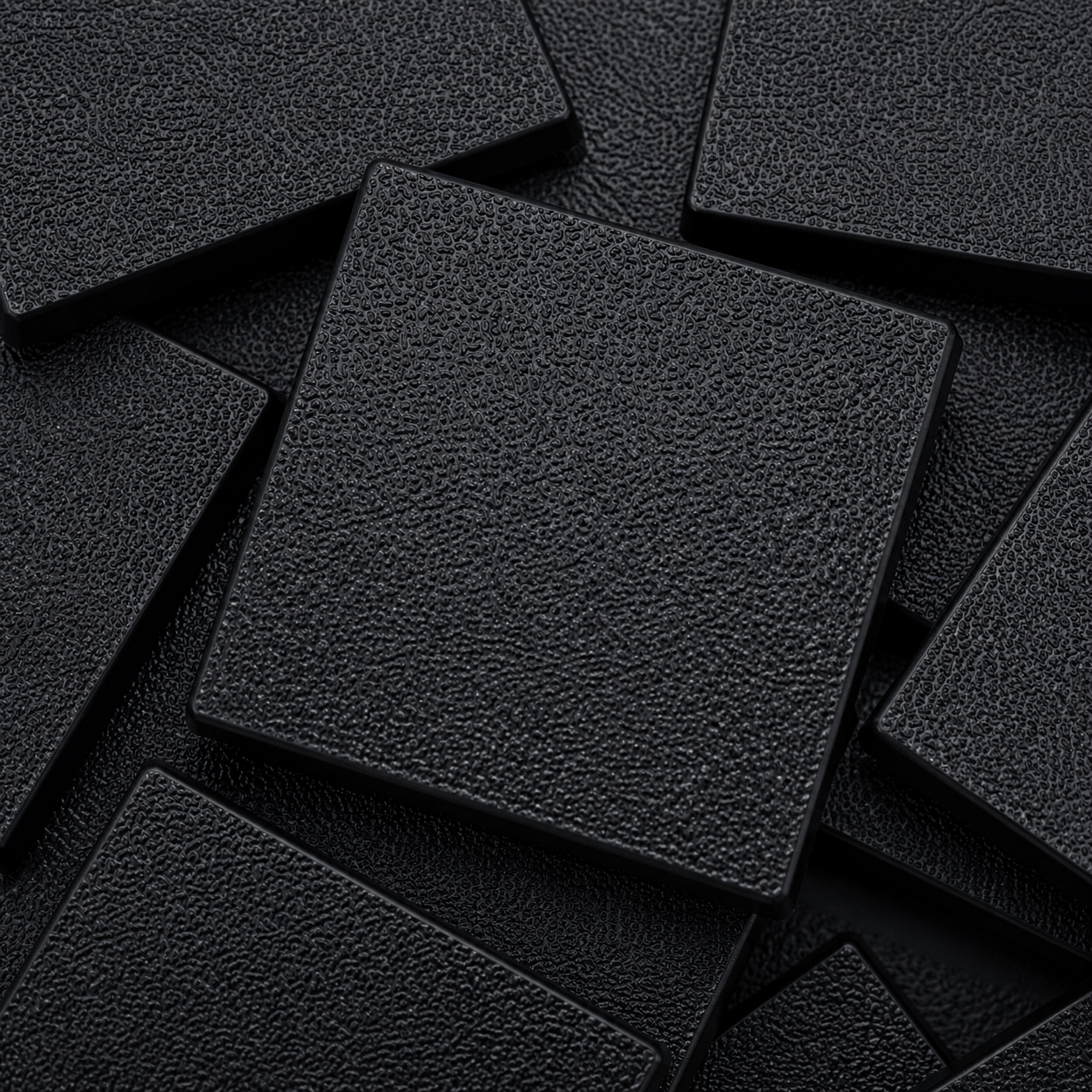 Close-up of black 40mm square plastic miniature bases showing textured top surfaces for tabletop wargaming, RPG monsters, rank-and-file units, conversions, and hobby basing projects.