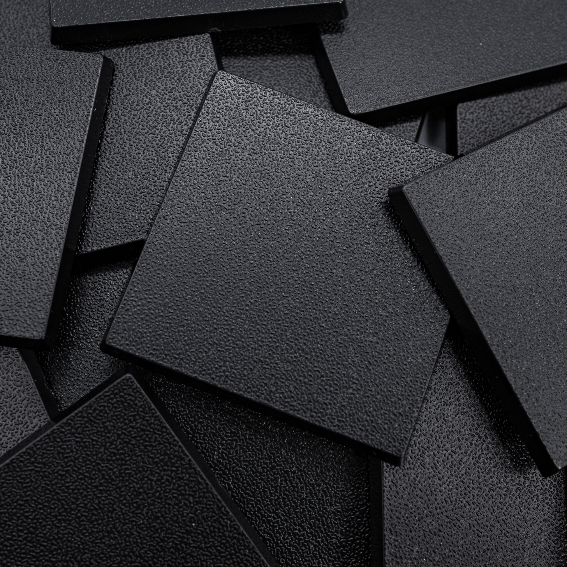 Close-up of black 50mm square plastic miniature bases showing textured top surfaces for tabletop wargaming, RPG monsters, rank-and-file units, conversions, and hobby basing projects.