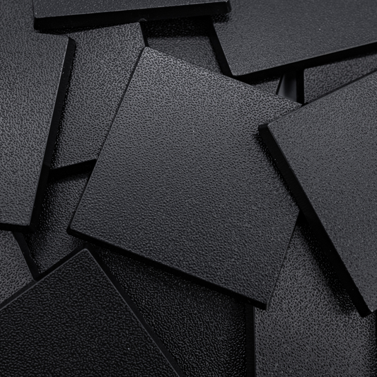 Close-up of black 50mm square plastic miniature bases showing textured top surfaces for tabletop wargaming, RPG monsters, rank-and-file units, conversions, and hobby basing projects.
