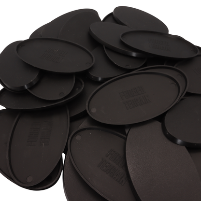 Underside view of black oval miniature bases showing the recessed base design and Forged Terrain branding.