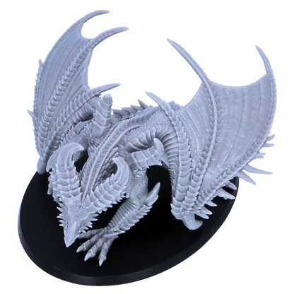 Top view of an unpainted Adult Iron Dragon miniature showing wing span, horn placement, spiked back details, and oval base shape.