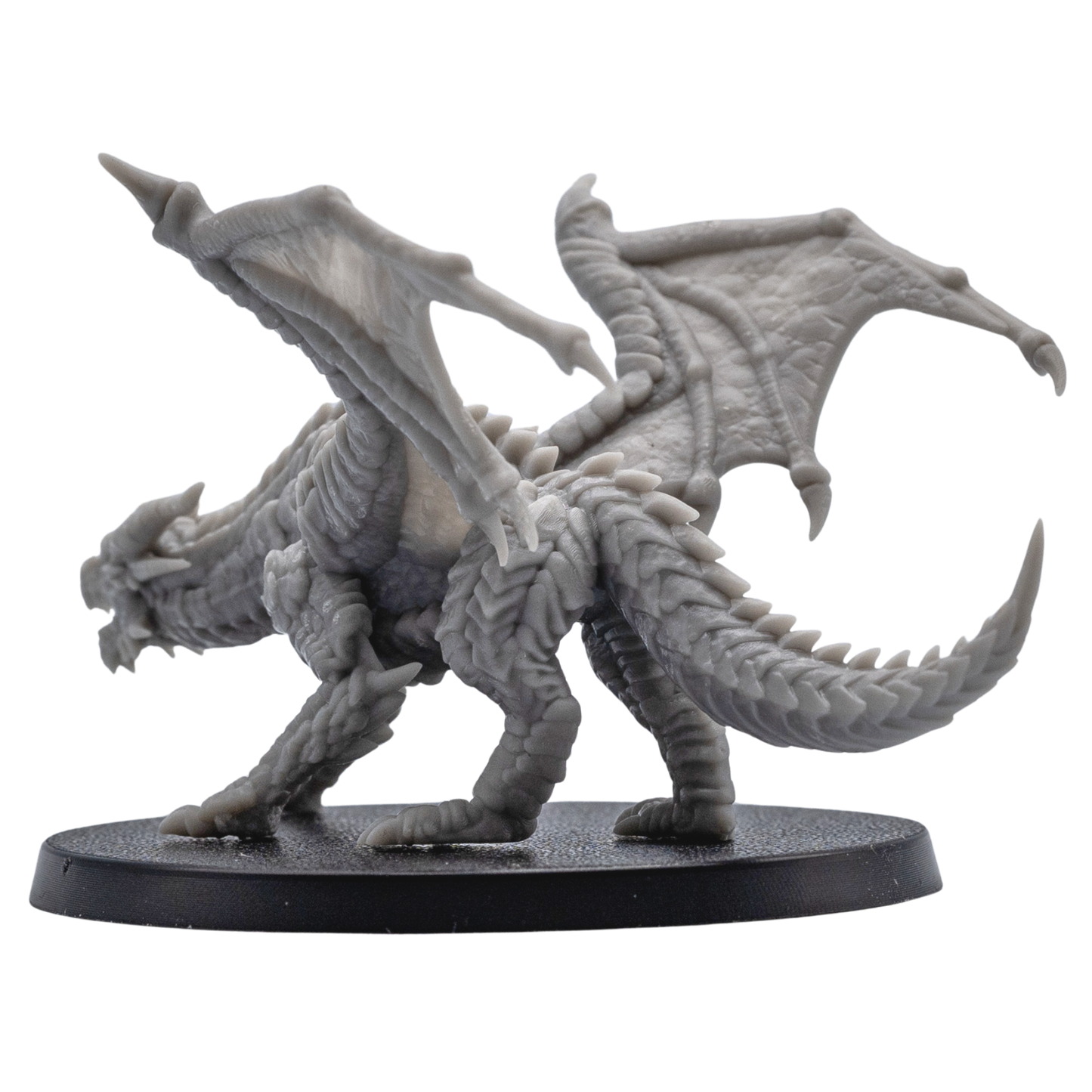 Rear side view of an unpainted Young Red Dragon miniature showing raised wings, scaled tail, claws, and 60mm round base.